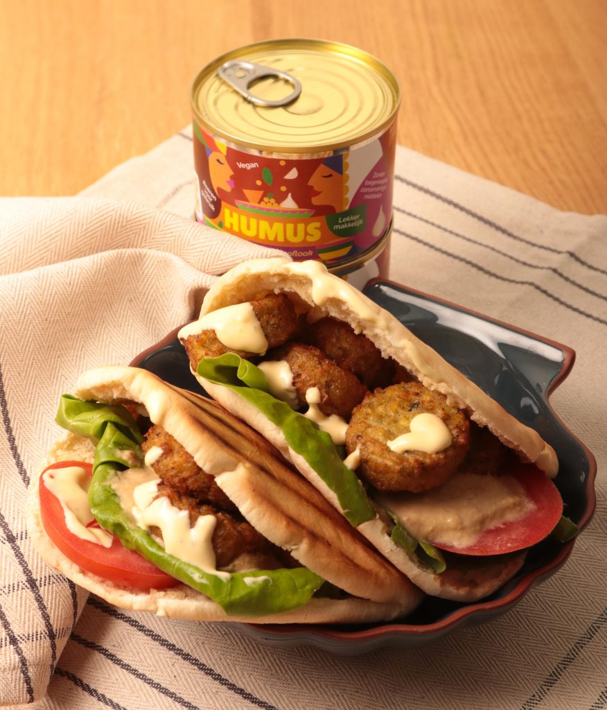Mixblik kleine humus blik op tafel naast een falafel gevulde pitabroodje.