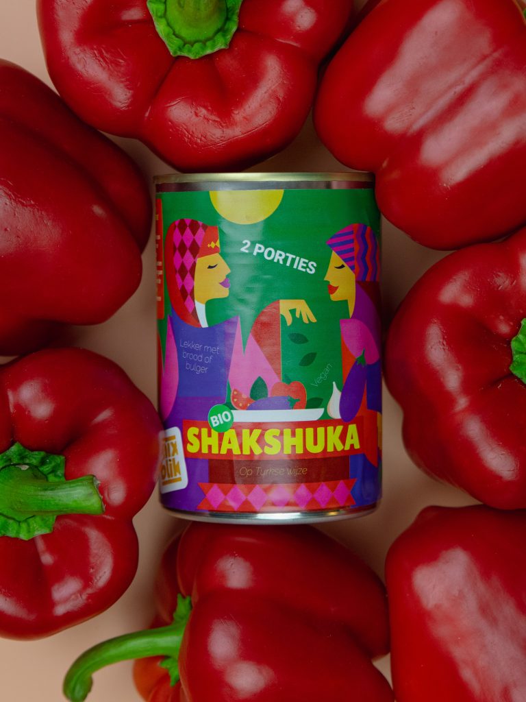 Mixblik Shakshuka blik met rode pepers op de achtergrond.